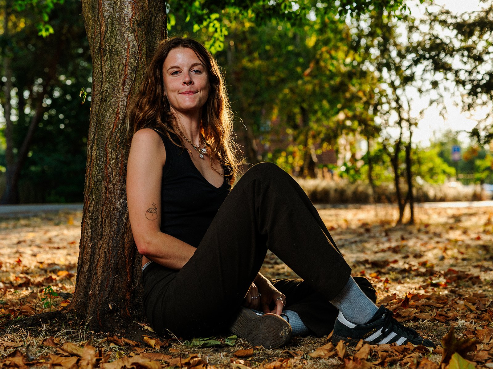 A young woman photographed sitting in London Fields park in East London as the late summer sun sets and shines through her blonde hair.