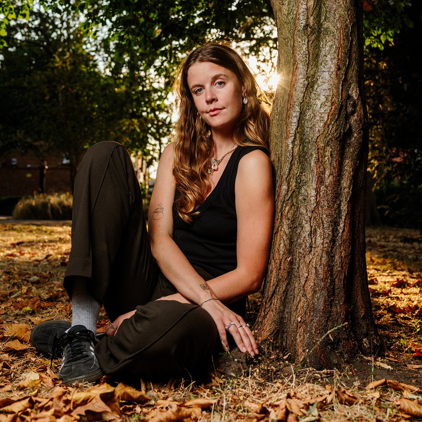 A young woman photographed sitting in London Fields park in East London as the late summer sun sets and shines through her blonde hair.