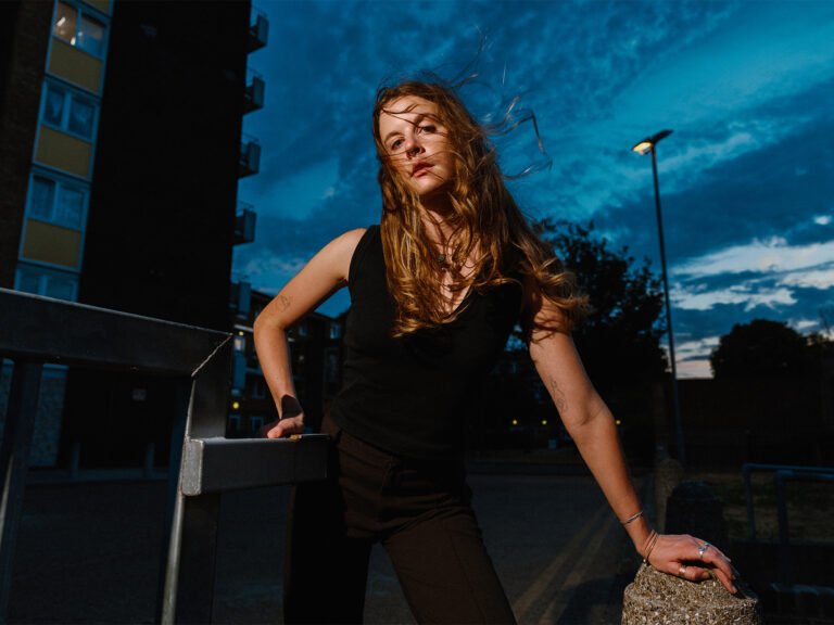 Portrait of a young woman in London Fields in East London at dusk, as wind blows through her blond hair.