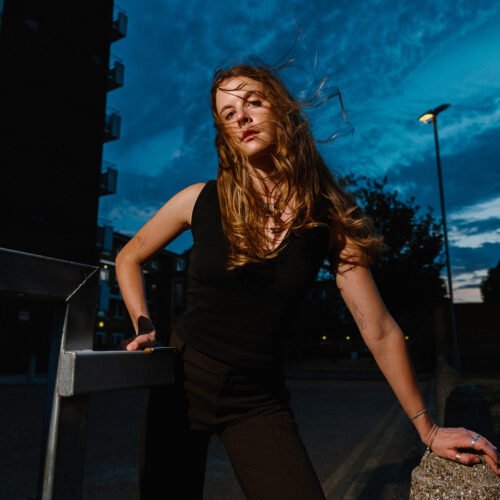 Portrait of a young woman in London Fields in East London at dusk, as wind blows through her blond hair.