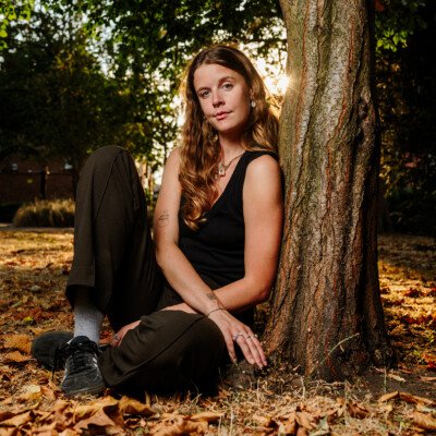 A young woman photographed sitting in London Fields park in East London as the late summer sun sets and shines through her blonde hair.