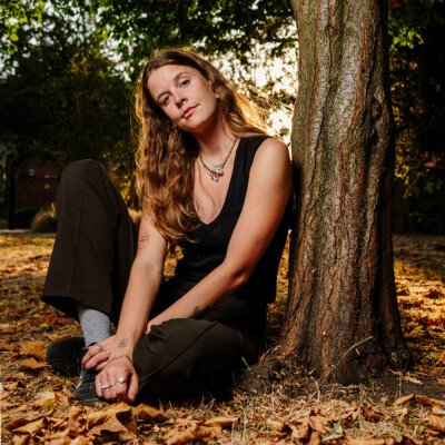 A young woman photographed sitting in London Fields park in East London as the late summer sun sets and shines through her blonde hair.