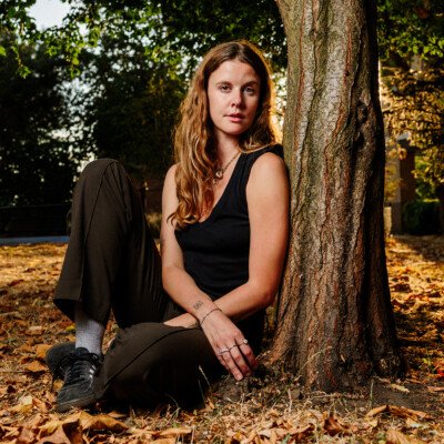 A young woman photographed sitting in London Fields park in East London as the late summer sun sets and shines through her blonde hair.