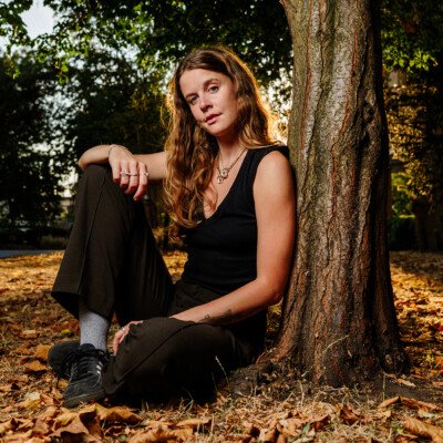 A young woman photographed sitting in London Fields park in East London as the late summer sun sets and shines through her blonde hair.
